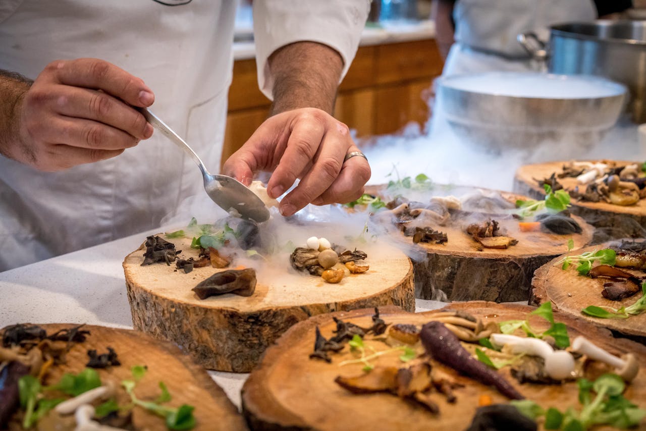 portfolio-01 A chef artfully plating a gourmet dish with mushrooms and greens on wood slices.